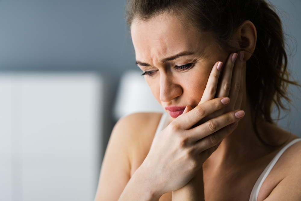 Woman holding her cheek in pain, looking distressed, demonstrating the need for methods on how to soothe wisdom tooth pain at home