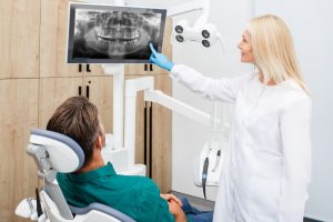 Dentist showing a patient an X-ray image of their teeth on a screen, discussing how to soothe wisdom tooth pain and possible treatment options.
