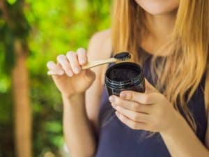 Woman using bamboo toothbrush with activated charcoal powder for natural teeth whitening in an outdoor setting.