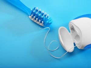 Toothbrush and dental floss on blue background, essential for preventing crooked teeth through proper oral hygiene.