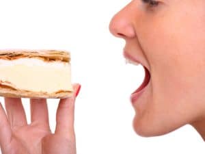 Close-up of a woman with a front dental implant, about to bite into a creamy dessert, showing her smile.