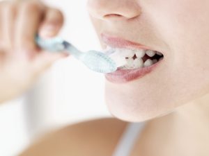 Person brushing teeth to prevent a dental crown falls off, highlighting good oral hygiene practices.