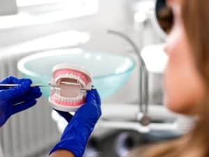 Dental professional showing denture model to patient, explaining denture pain causes and solutions.