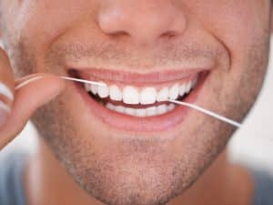 A person flossing to maintain good oral hygiene, essential for ensuring the longevity of different types of dental implants.