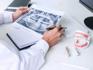 Dental X-ray analysis showing an infected tooth extraction plan with dental models and tools on a desk.