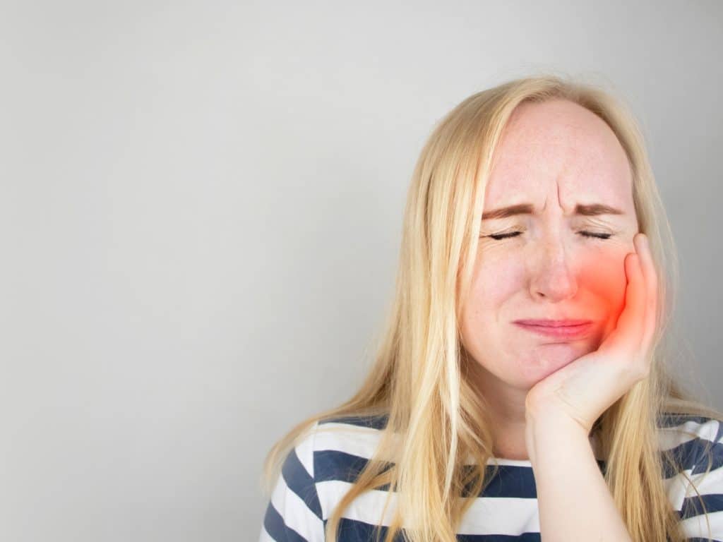 Person experiencing tooth pain from hot food, holding jaw in discomfort while eating