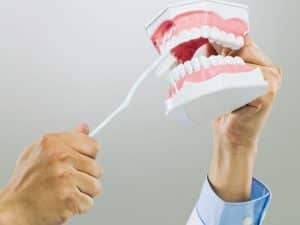 Brushing dentures with a toothbrush to prevent denture discomfort caused by poor hygiene and plaque buildup.