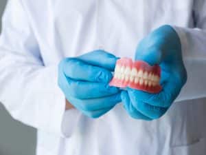 Dentist in gloves holding full dentures, highlighting causes of denture discomfort and the need for proper fit.