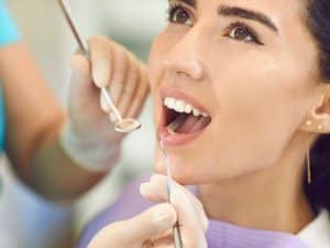 Woman at a dental check-up with a dentist examining her teeth. Seeking solutions when teeth feel rough post-treatment.