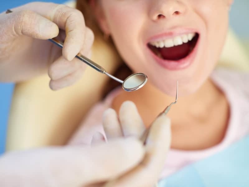 Close-up of a dentist performing preventive dental treatment with a mirror and probe on a patient's open mouth.