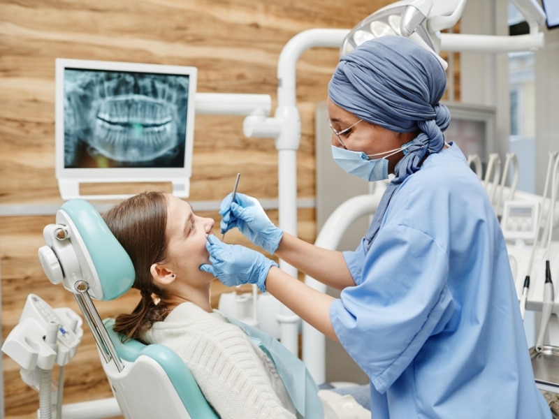 Dentist examining female patient during routine check-up, reinforcing importance of a consistent dental schedule.
