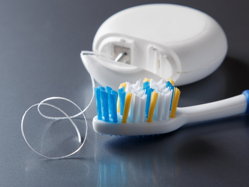 Toothbrush and dental floss on table representing essential care after cosmetic dentistry procedures.