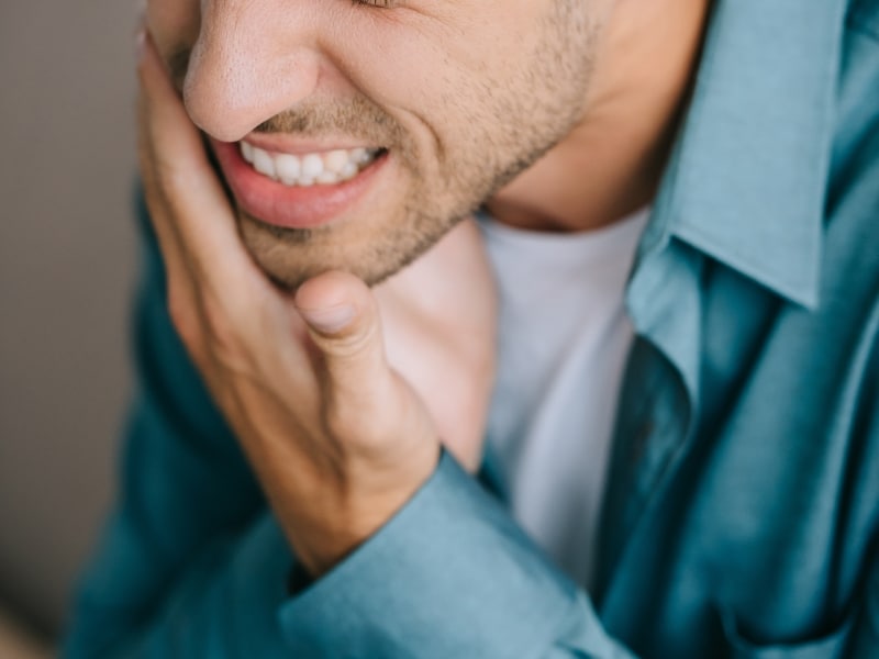 Man holding his cheek in discomfort caused by poor oral health problems.